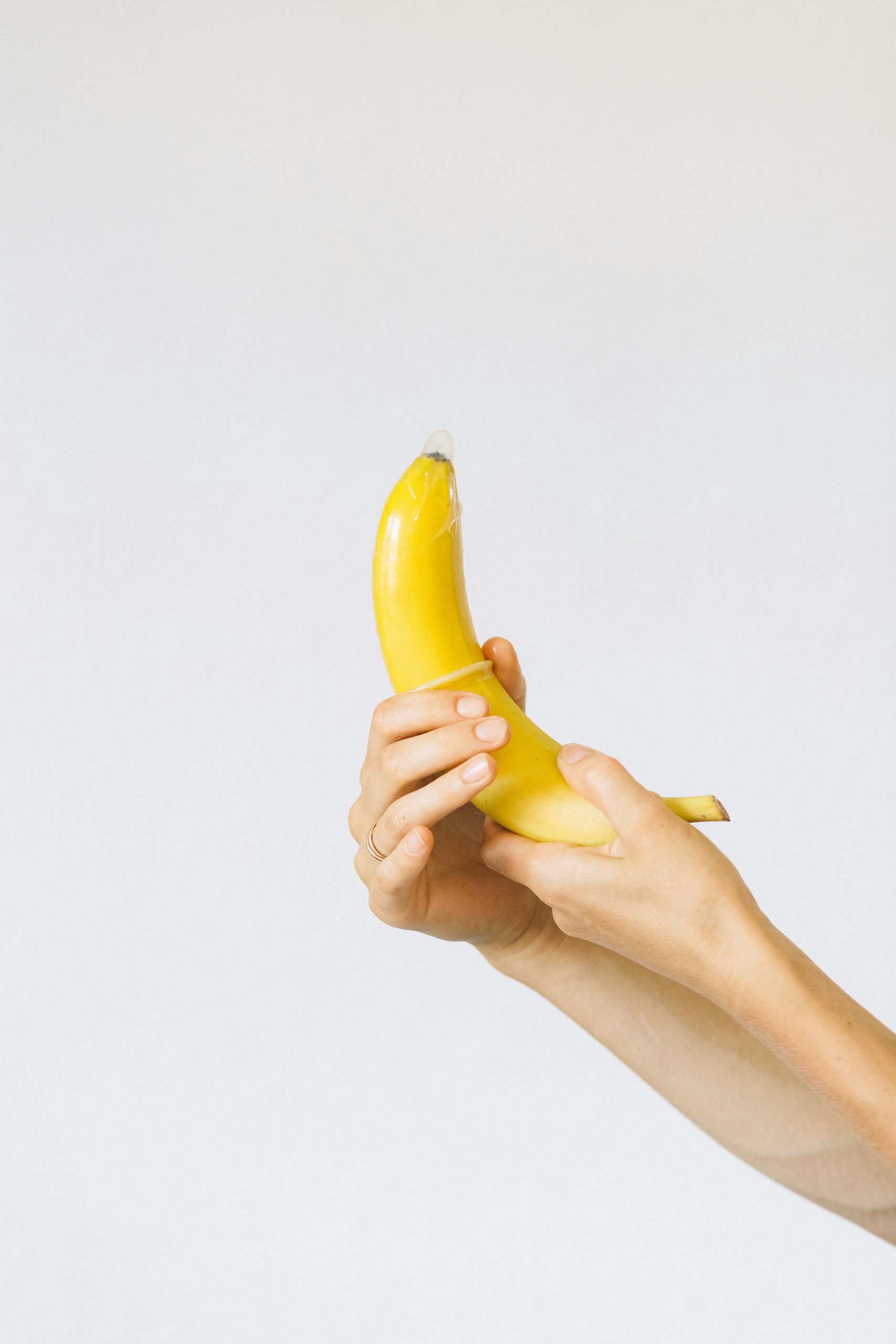 A banana held in hands with a condom on top symbolizes safe sex education.